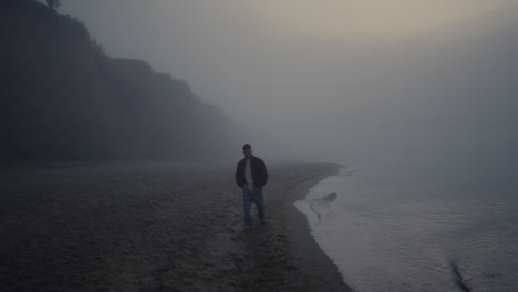 lonely guy walking beach in foggy sunrise morning. man exploring nature in mist