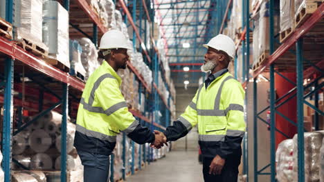 two warehouse workers shaking hands in a warehouse aisle