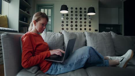 mujer trabajando en una computadora portátil en un sofá en una sala de estar