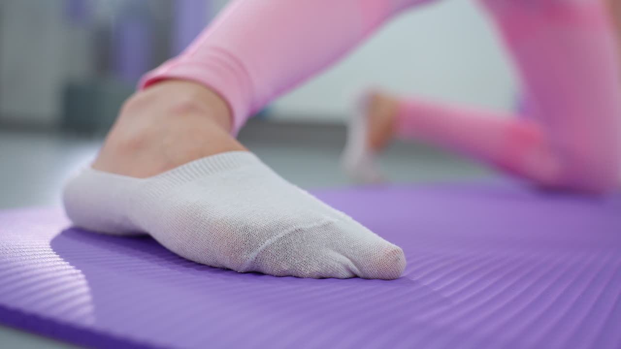 보라색 운동 매트 위에 색 스포츠 양말을 입은 발의 클로즈업, 운동 세션 중에 스트레칭, 다른 다리가 매트에 무을 고 배경에 약간 흐릿하게 나타납니다.