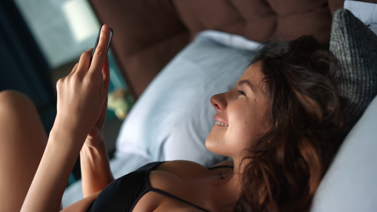 una mujer bonita arrojando un teléfono móvil a la cama.