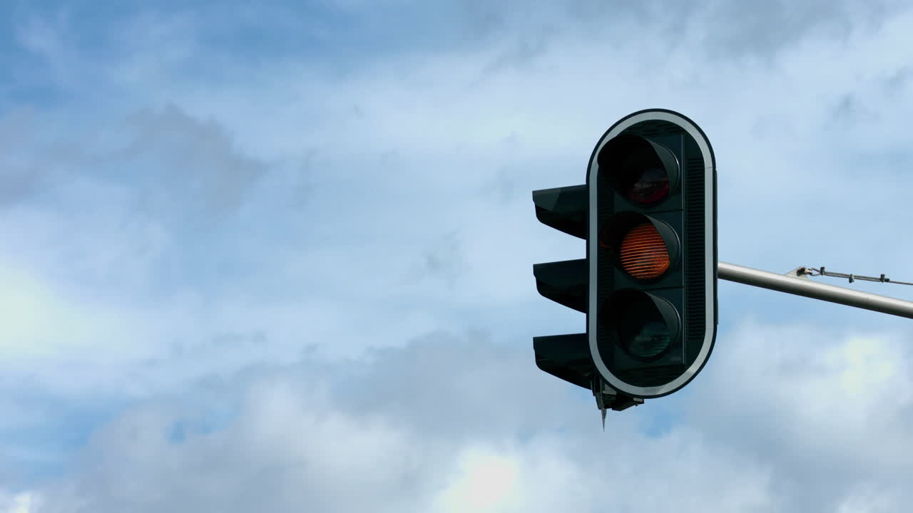 Traffic light changing from orange to red, over sky background