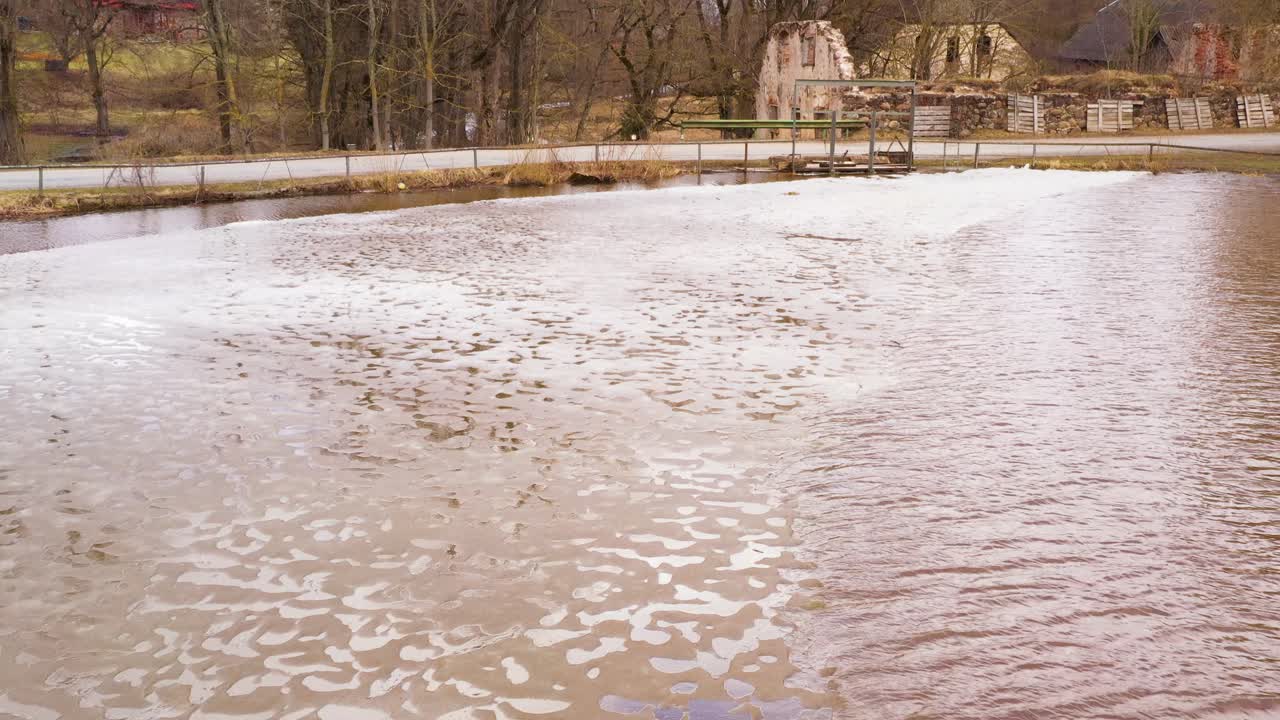 Frozen part of dam water near abandoned building, aerial drone view
