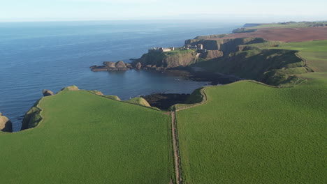 aerial view of the green fields at the scottish shore to the ocean with in the distance the ruins of the medieval castle of dunnottar