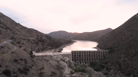 drone flying over a valley, approaching a dam and lake