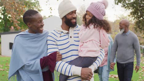 video of happy african american parents walking in garden holding daughter with grandparents behind