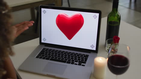 animation of heart over african american woman drinking wine and using laptop with copy space