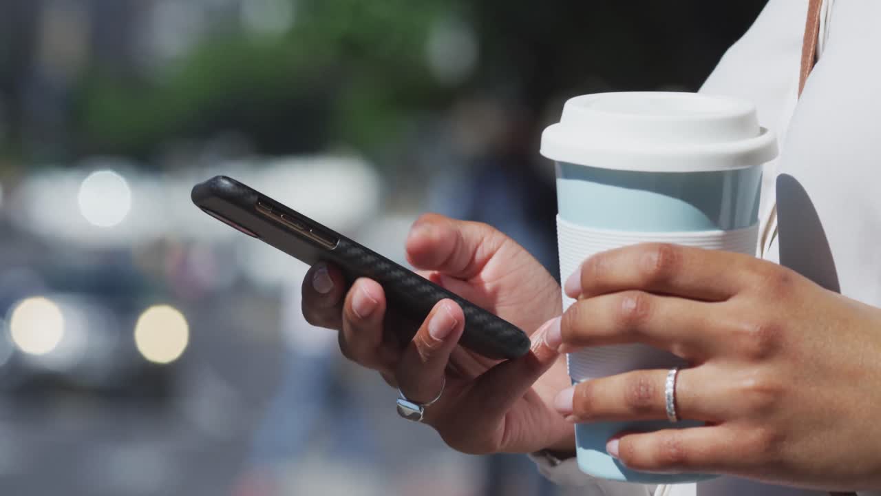 Midsection of african american woman using smartphone and holding coffee in street
