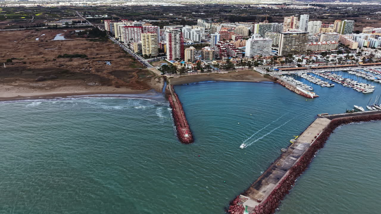 Vista costiera al tramonto che mostra edifici sul lungomare, porto e barche in una trafficata area portuale vicino alla spiaggia in una città di mare.