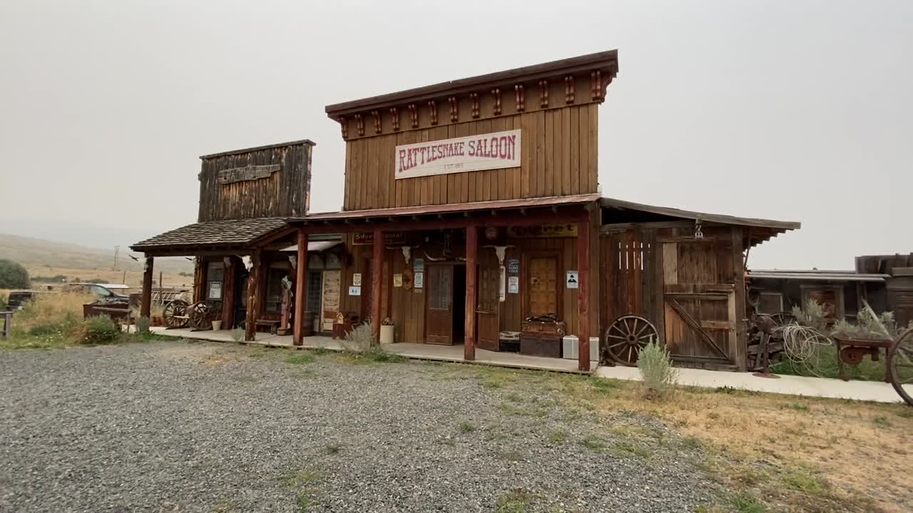 Saloon stands with rustic wood design, wagon wheel decor, gravel path, and faded sky, reflecting quiet charm of historical West Virginia countryside structure