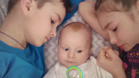 siblings with baby on bed. close up of brother and sister kiss newborn baby boy