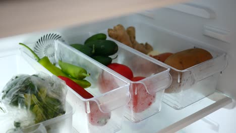 person reaching into refrigerator to grab red pepper