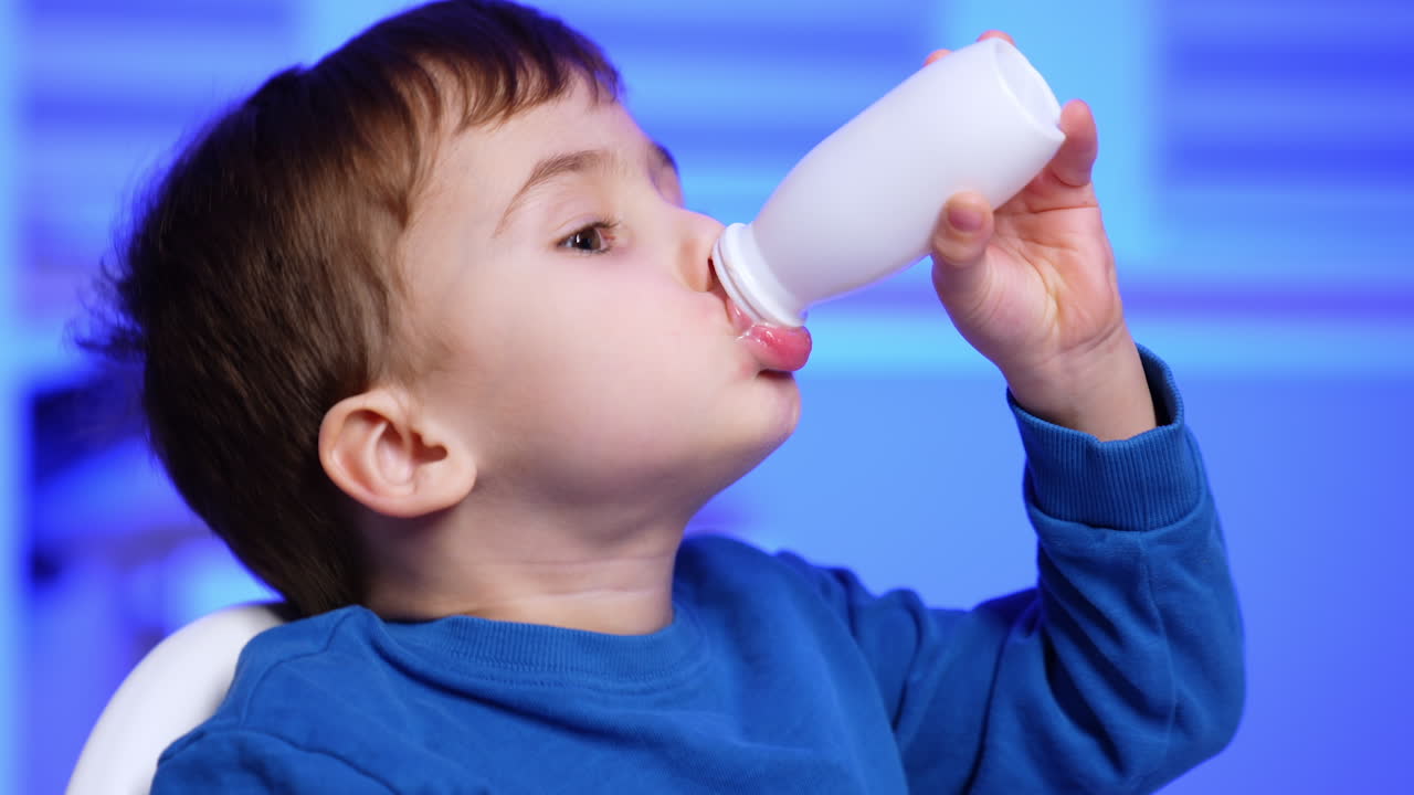 Small kid tries to get the latest drop of yogurt form a bottle. Portrait of a child eating dairy. Close up.