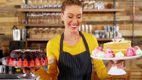 Portrait-of-waitress-holding-cake-in-cake-stand-at-cafÃ©