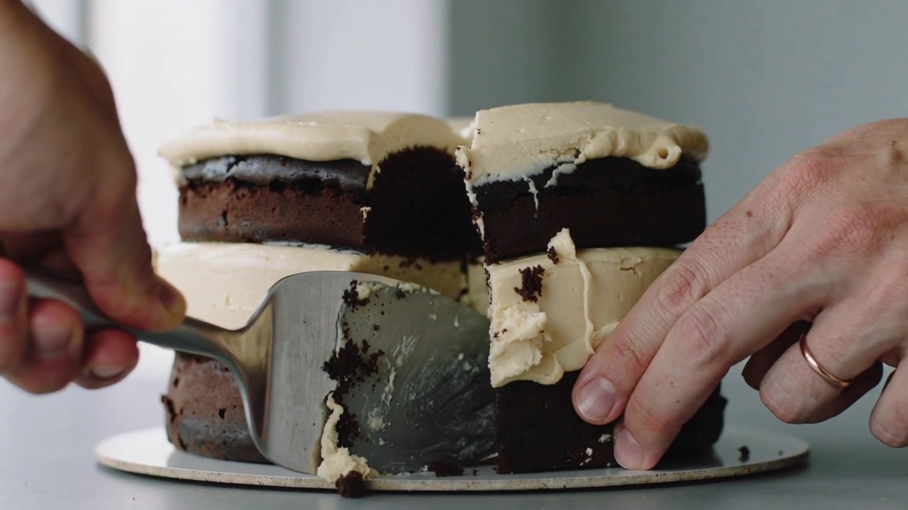 Inserindo espátula no bolo, mãos de adulto cortando o centro de um bolo de chocolate no balcão para servir.