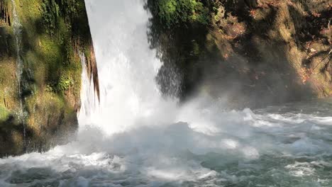 raging crystal clear waterfall empties into a pool of water at the bottom of a mossy cliff wall creating a beautiful oasis like setting