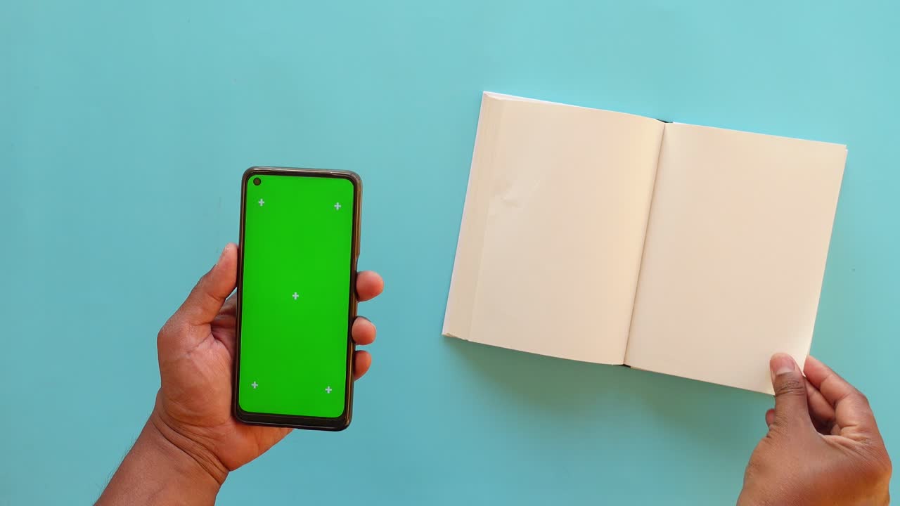 Persona che tiene un telefono con schermo verde e un libro aperto