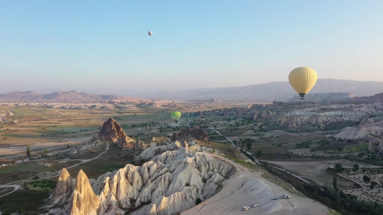 Ampia vista aerea con drone di molteplici mongolfiere che fluttuano nel cielo sopra il drammatico paesaggio vallivo della Cappadocia, Nevsehir, Turchia, all'alba
