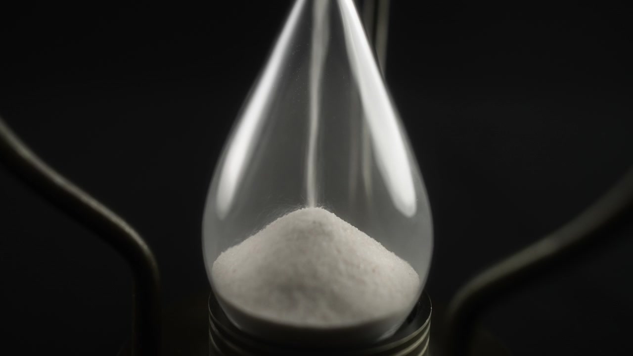 Close-up of White Sand Flowing Through a Glass Hourglass