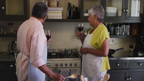 una pareja biracial está bebiendo vino y disfrutando preparando comida en la cocina.
