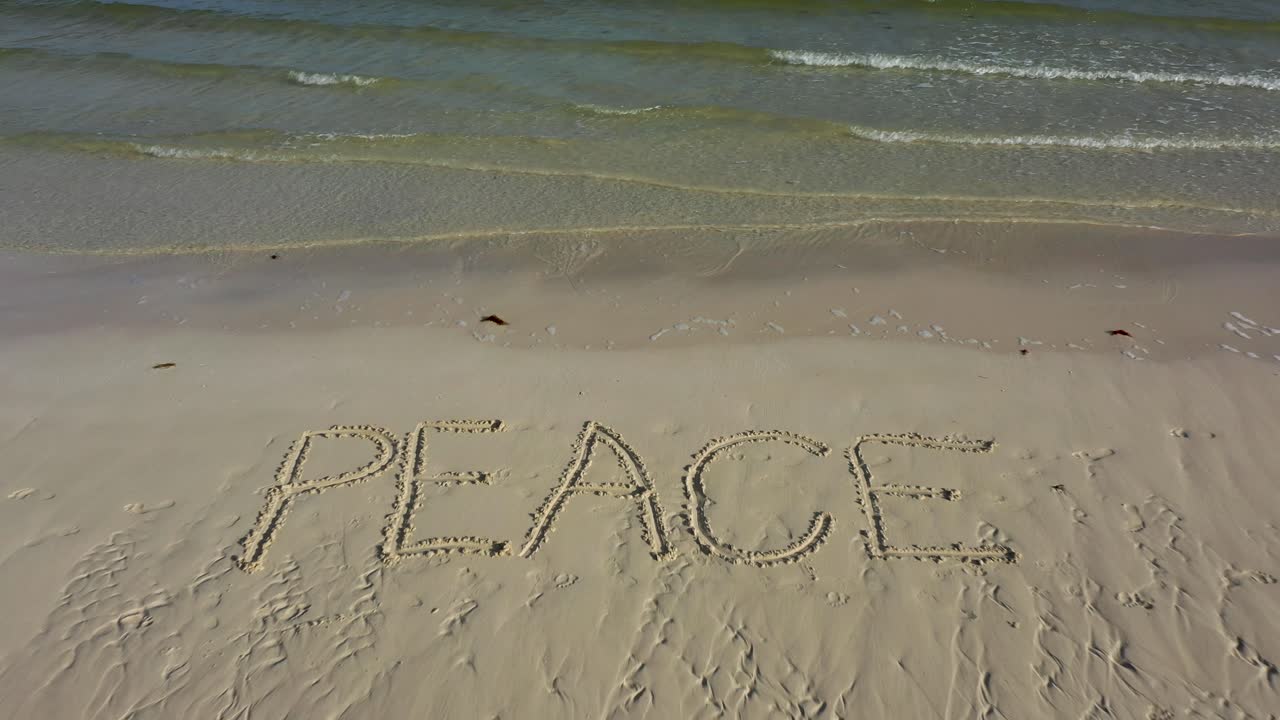 Aerial camera looking straight down showing PEACE inscribed into the sand on a beach