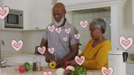 animation of pink hearts over happy african american senior couple preparing food in kitchen