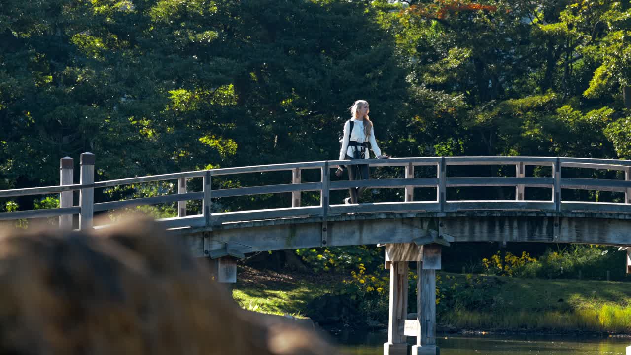 A tranquil moment featuring a girl strolling on a traditional bridge, taking in the serene view of the lake at Hamarikyu Gardens in Tokyo.