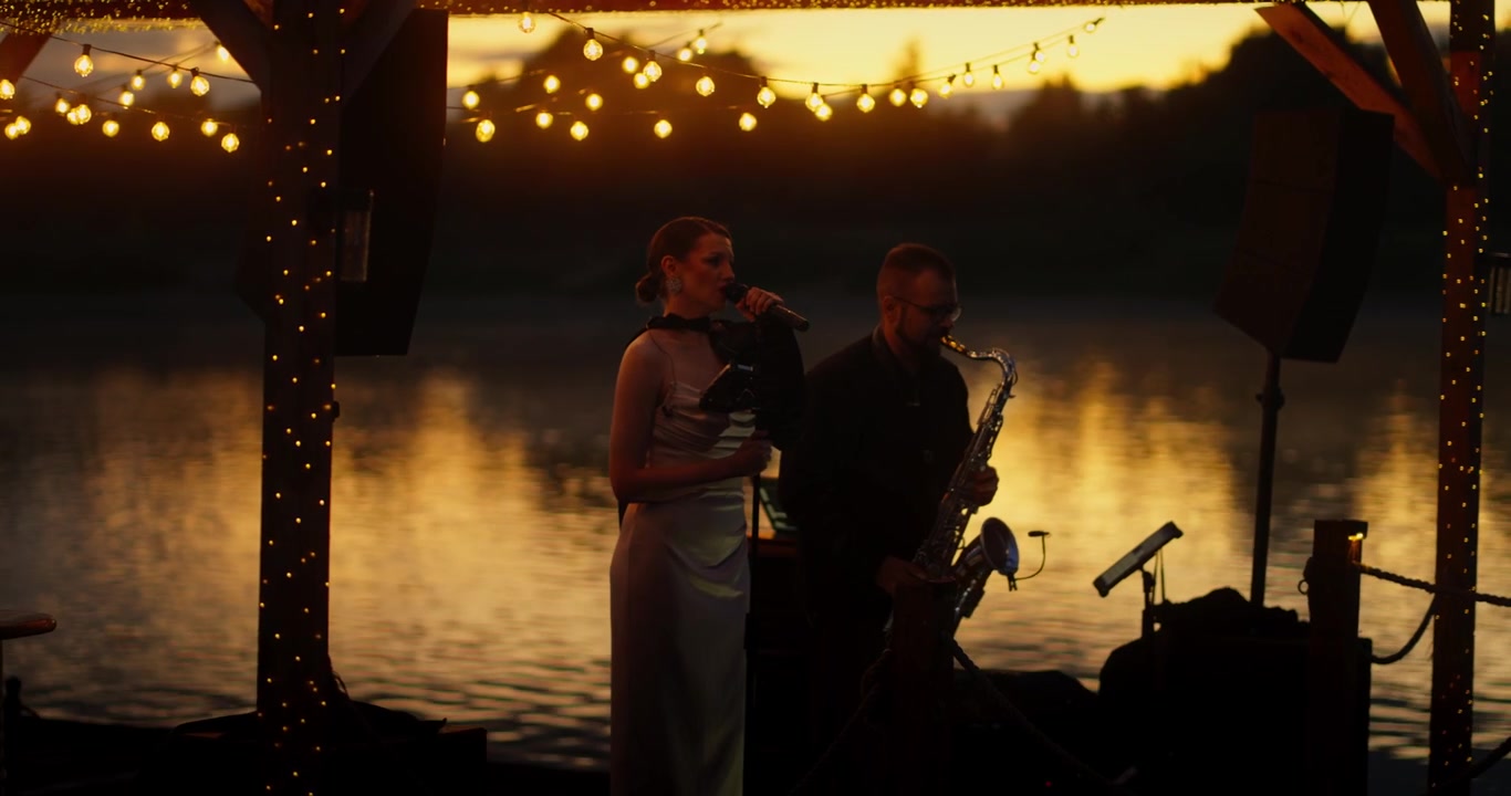 Muzikanten spelen livemuziek op een podium aan het meer bij zonsondergang