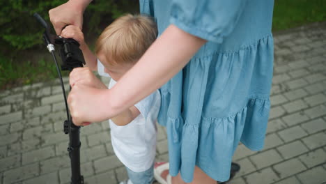 a close-up of a mother guiding her young son on a scooter ride, the child s small hands hold the handlebar tightly as the mother provides steady support