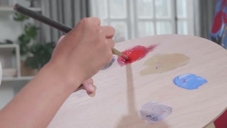 cerca de una mano que sostiene un pincel y lo mezcla con color antes de pintar