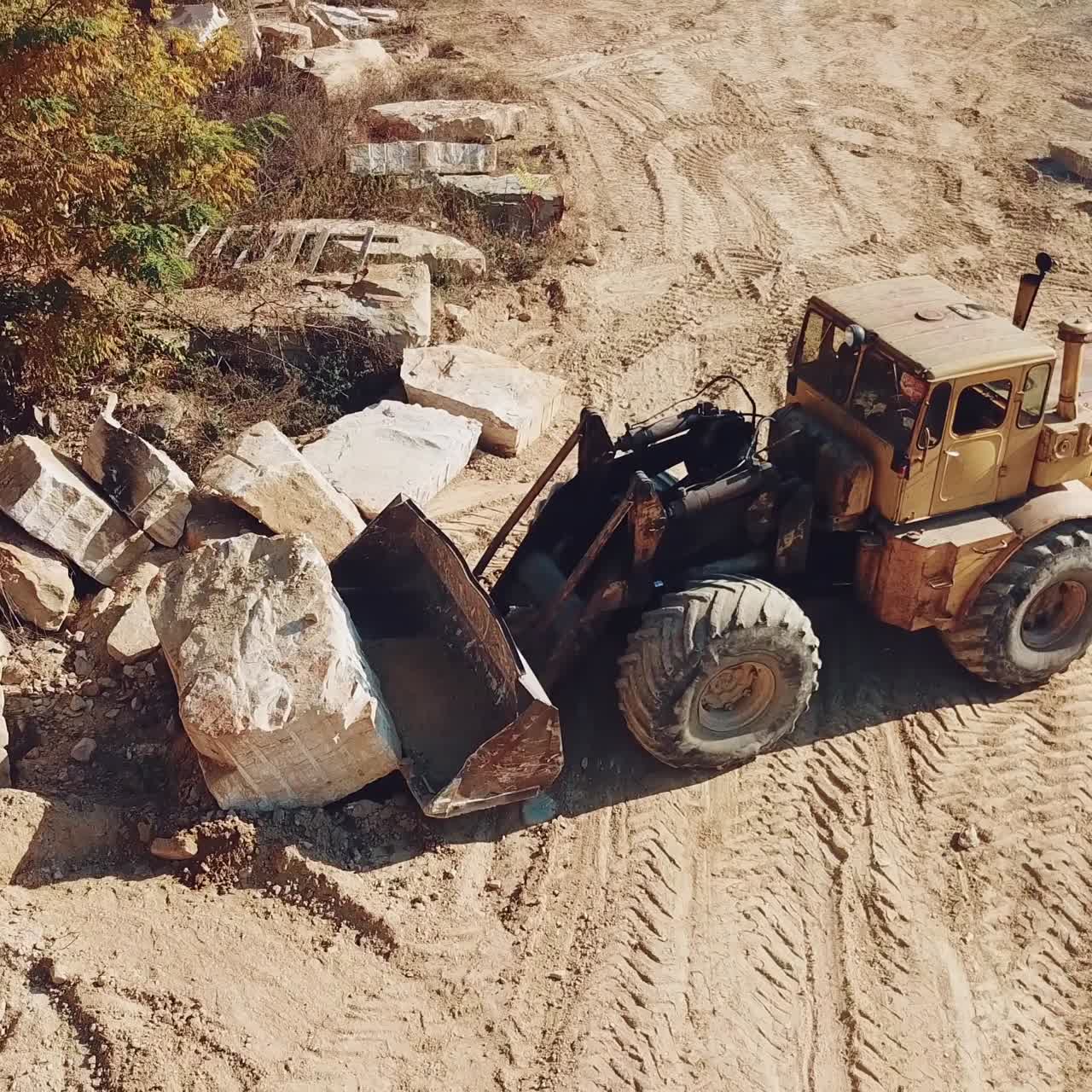professional equipment with a bucket is turning over a stone and raising it near sandy quarry on the background of trees. Close-up