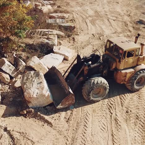 professional equipment with a bucket is turning over a stone and raising it near sandy quarry on the background of trees. close-up