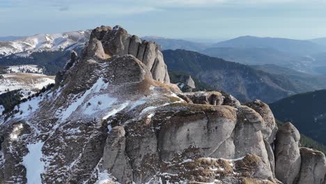 Montañas-Ciucas-Cubiertas-De-Nieve-Bajo-Un-Cielo-Azul,-Picos-Escarpados-Con-Bosques-De-Pinos-En-El-Fondo,-Toma-Aérea