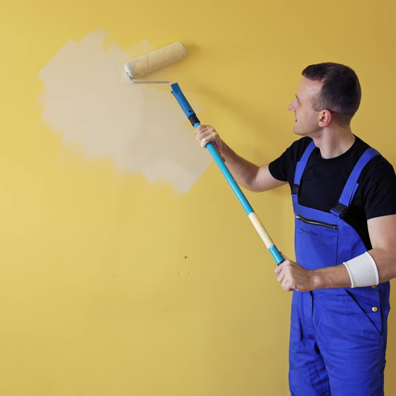 Room renovations at home. Painter man starts painting wall with a roller on a long handle. Professional painting services, contractor