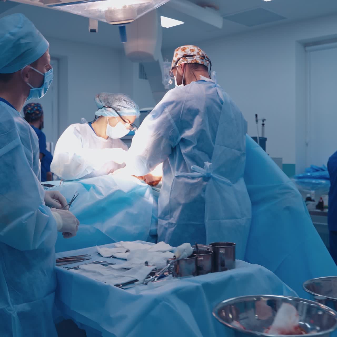 Team of surgeons doing plastic surgery in modern clinic. Group of medical workers in blue uniform perform an operation to a patient.