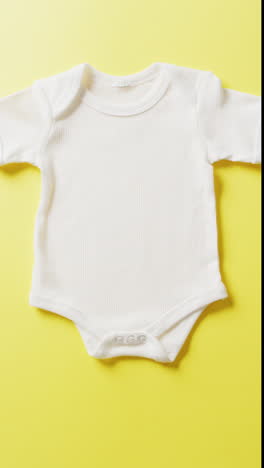 vertical video of close up of white babygrow on yellow background with copy space