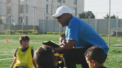 Niños-De-Fútbol-En-Círculo-Y-Escuchando-Al-Entrenador-En-Un-Día-Soleado