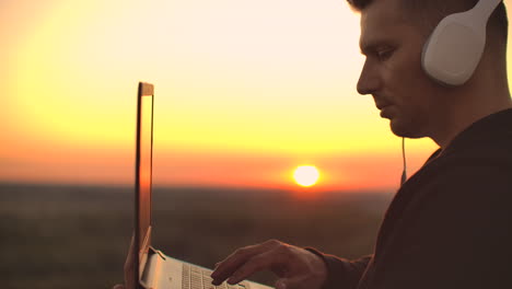 estar de pie al atardecer en el techo con una computadora portátil y cerveza en auriculares trabajar remotamente y contemplar la belleza. estar en armonía trabajar de forma remota con su computadora portable.