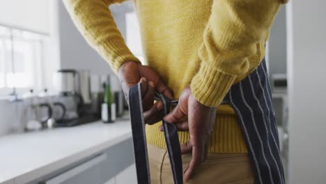 a senior african american man tying a kitchen apron. social distancing in quarantine.