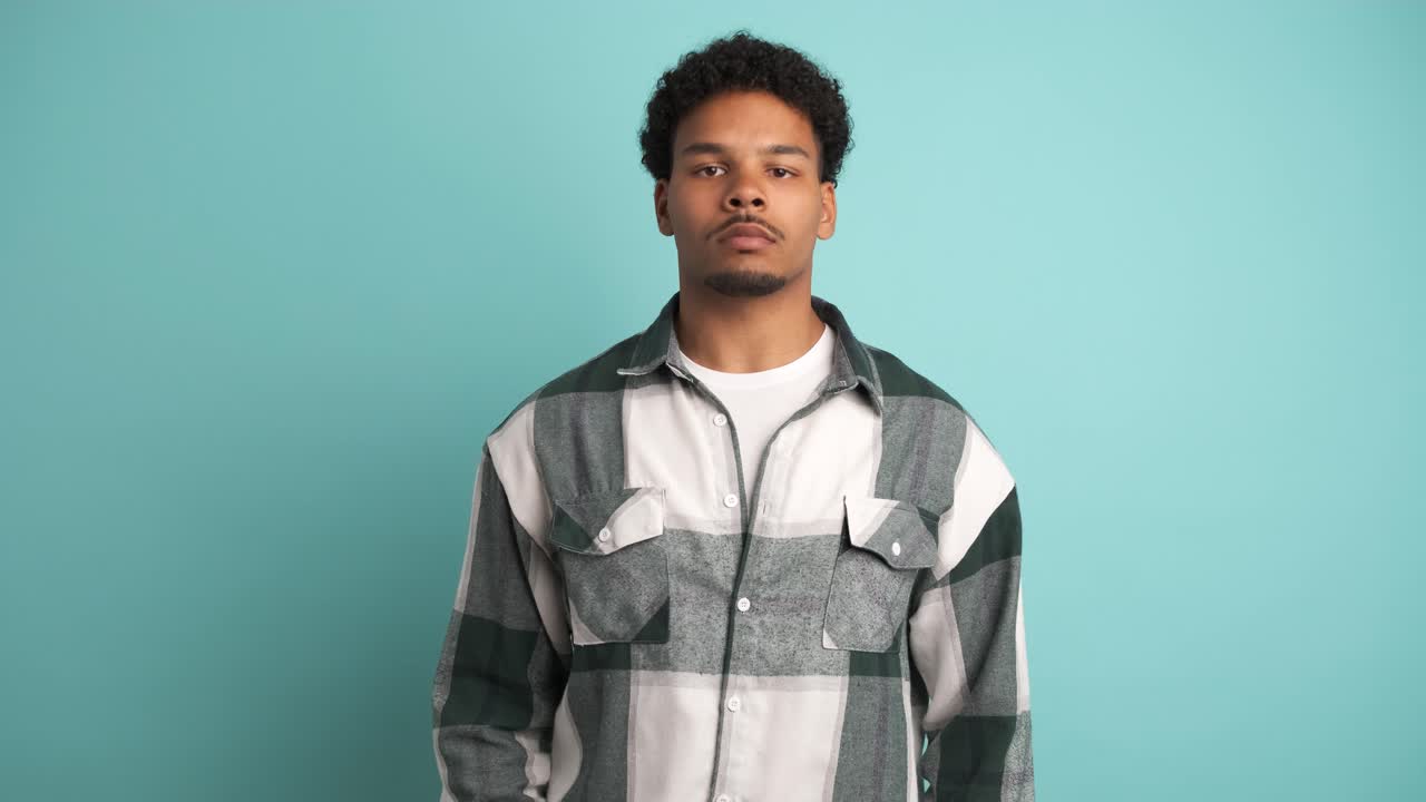Serious young man looking at camera in blue studio