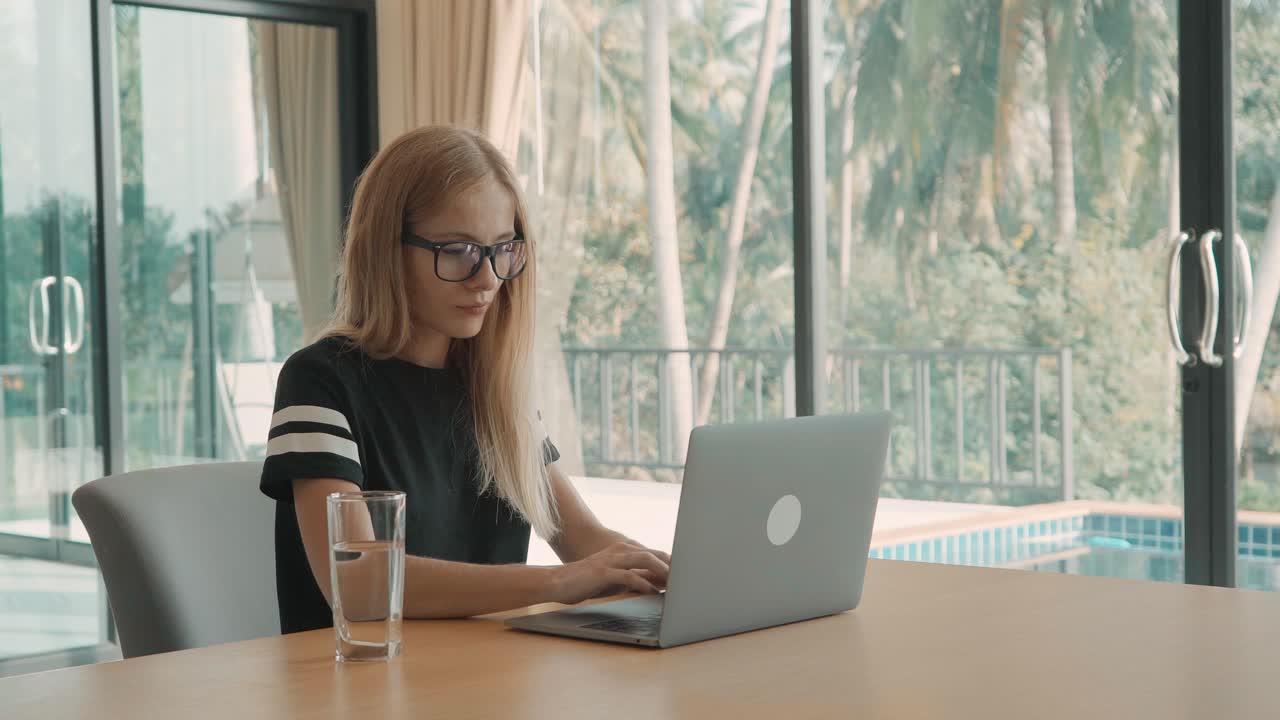 Junge Frau arbeitet am Laptop in tropischer Wohnumgebung