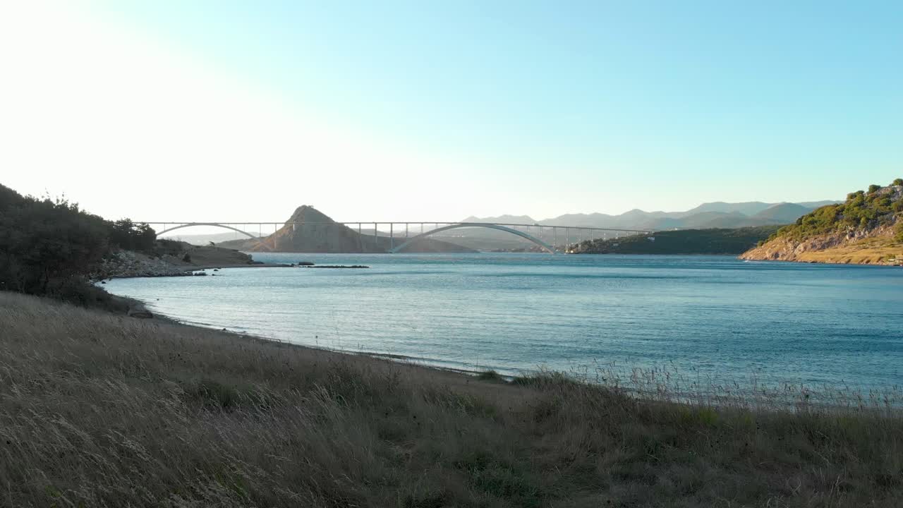 가벼운 바람이 베이를 가로질러 불 때 크르크 다리의 풀로 뒤덮인 해안 위로 공중이 드러납니다.