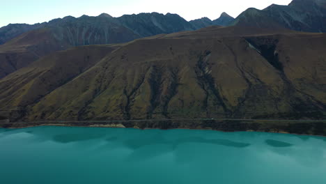 vista aérea de un avión no tripulado rastreando un coche que conduce a lo largo de una pintoresca carretera de montaña a lo largo de un lago glacial turquesa