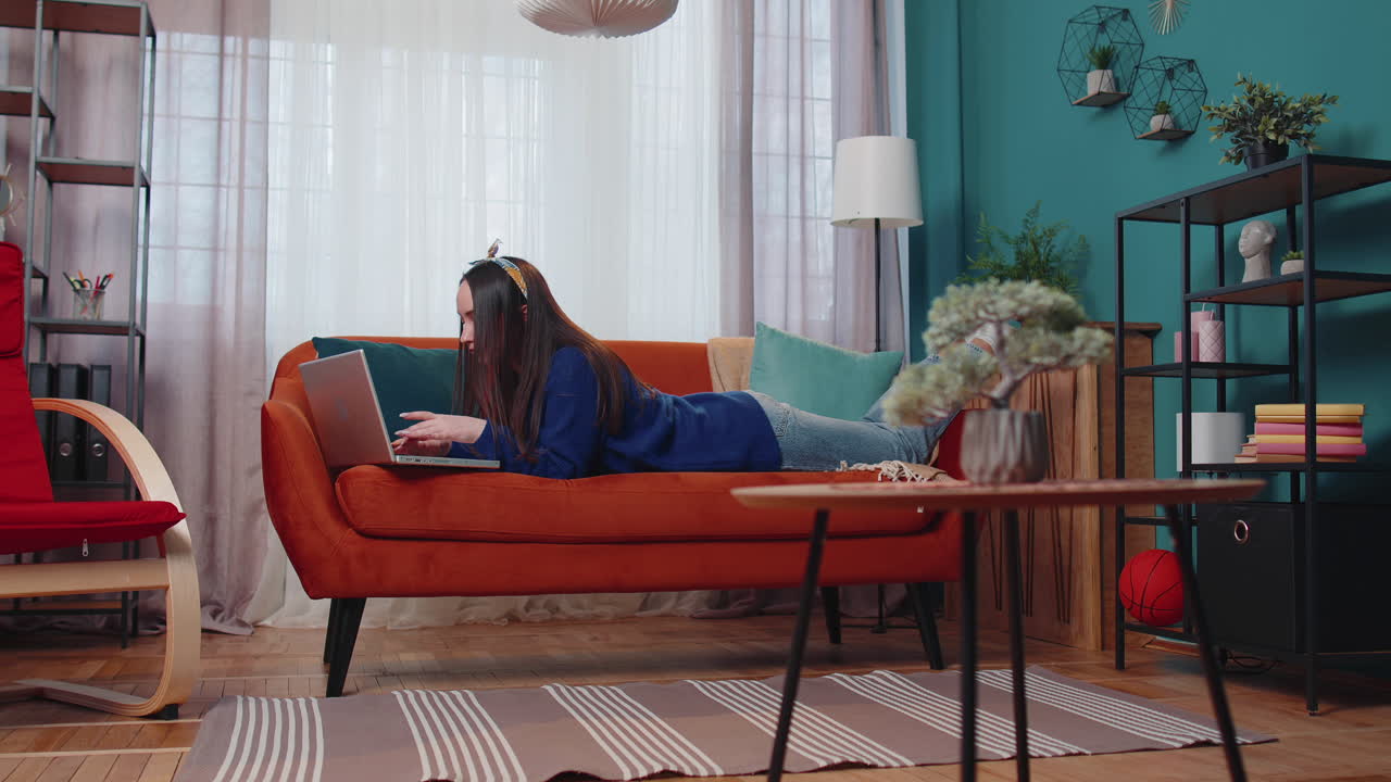 소파에 누워있는 즐거운 젊은 여성, 노트북 pc를 사용하여 소셜 미디어 응용 프로그램에서 메시지를 공유