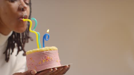 Close-Up-Studio-Shot-Of-Woman-Wearing-Birthday-Headband-Celebrating-Birthday-Blowing-Out-Candles-On-Cake