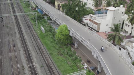 aerial shot of a biker going on a bridge near a railway track surrounded by buildings and trees