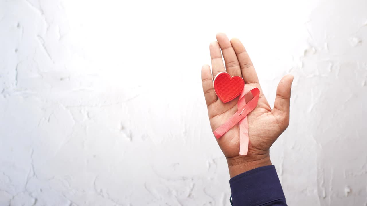 mano con cinta rosada y corazón para la concienciación sobre el cáncer de mama