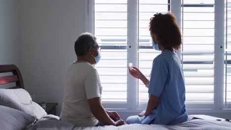 senior mixed race man with female doctor wearing face masks and holding pills