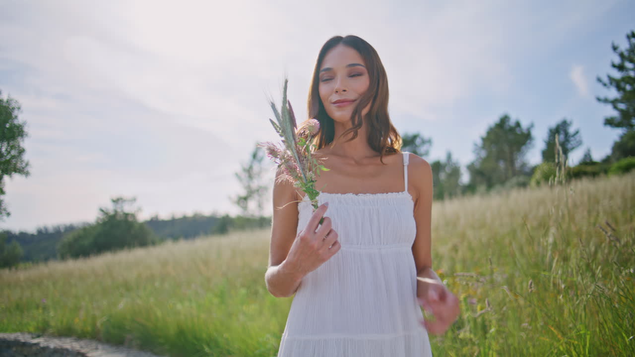 Coquettish girl sniffing wildflowers walking meadow closeup. Countryside woman
