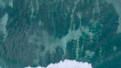 Vista-De-Arriba-Hacia-Abajo-En-Cámara-Lenta-Con-Drones-De-Aguas-Cristalinas-Y-Olas-Rompiendo-Sobre-Arrecifes-De-Coral-Poco-Profundos-En-Uluwatu-Bali-Indonesia